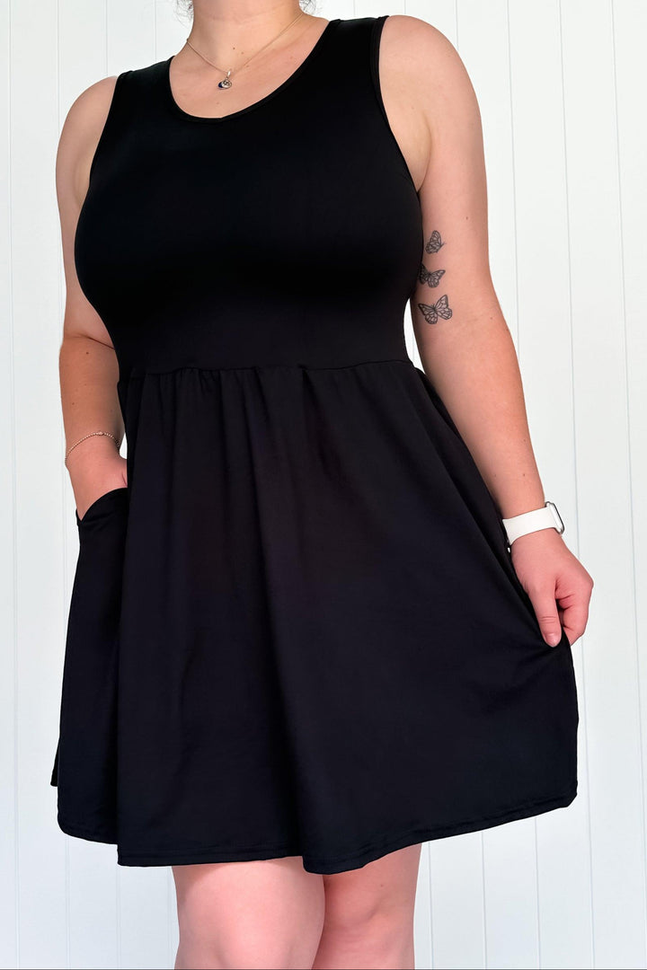 A model wearing a sleeveless black mini dress with pockets.