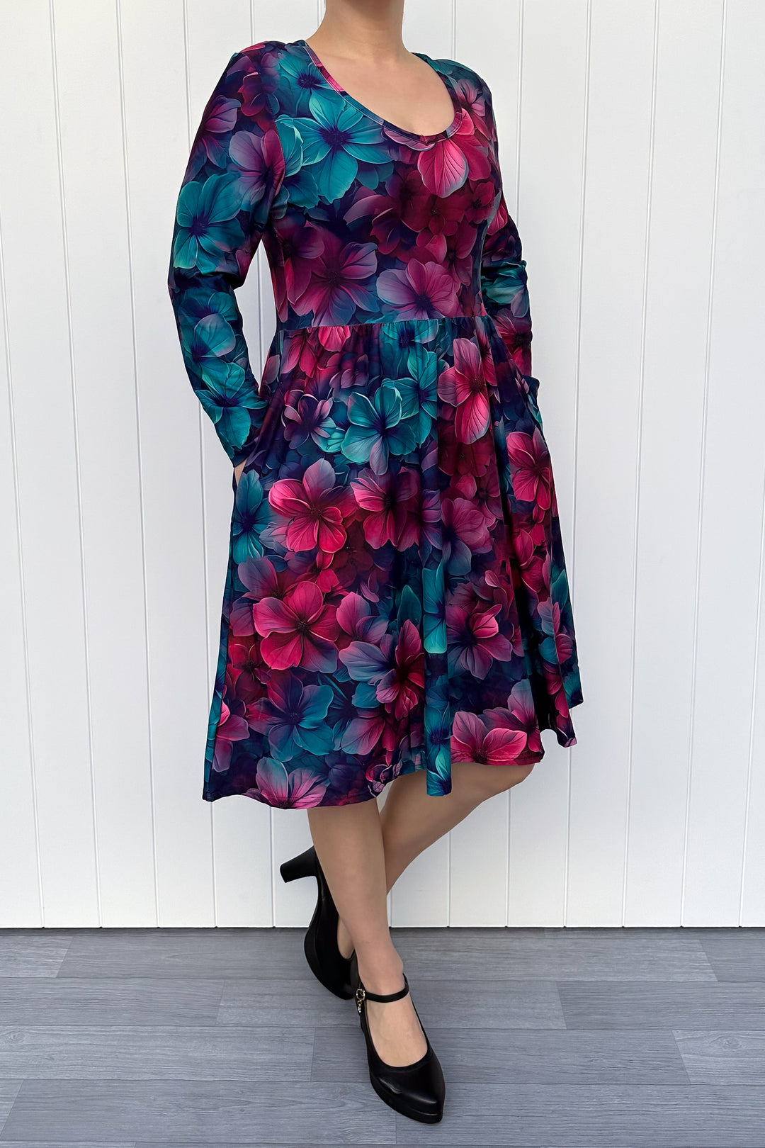 Woman wearing a colorful floral dress against a white wooden panel background