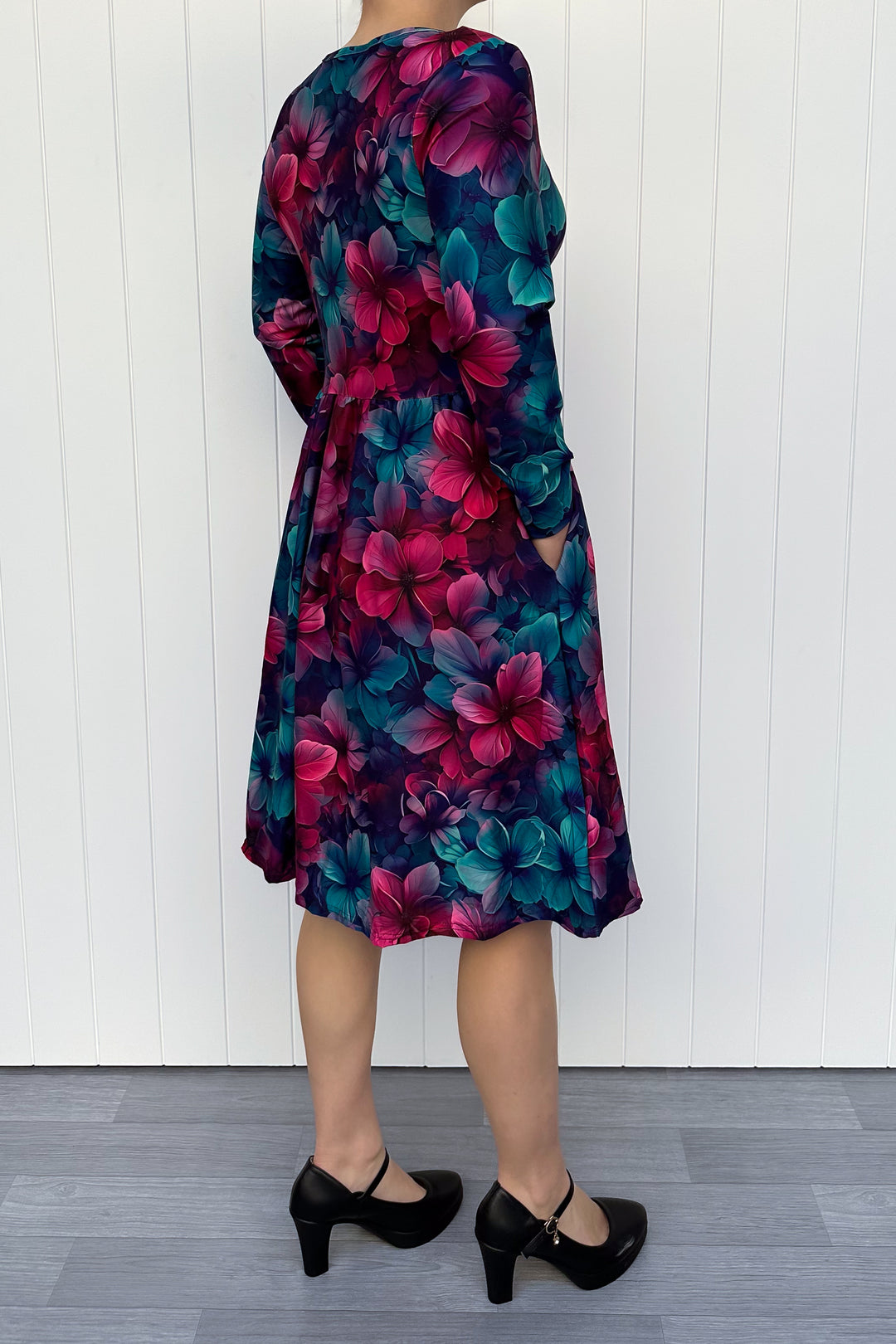Person wearing a red and teal floral dress with a white wooden background