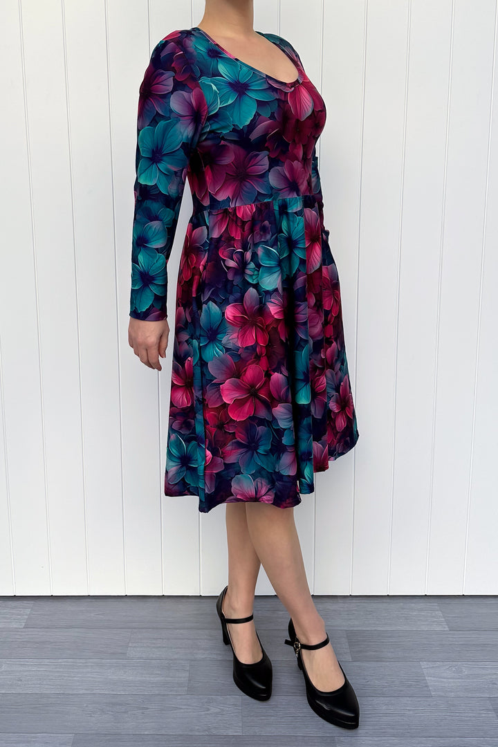 Person wearing a colorful floral dress against a white wooden panel background