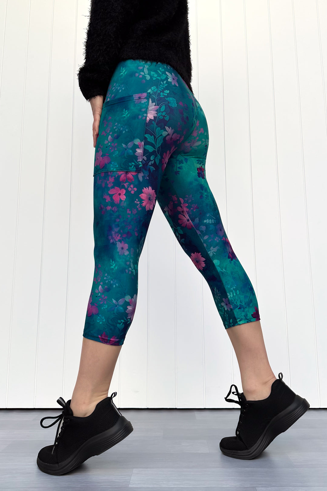Person wearing teal floral leggings with black shoes on a white background