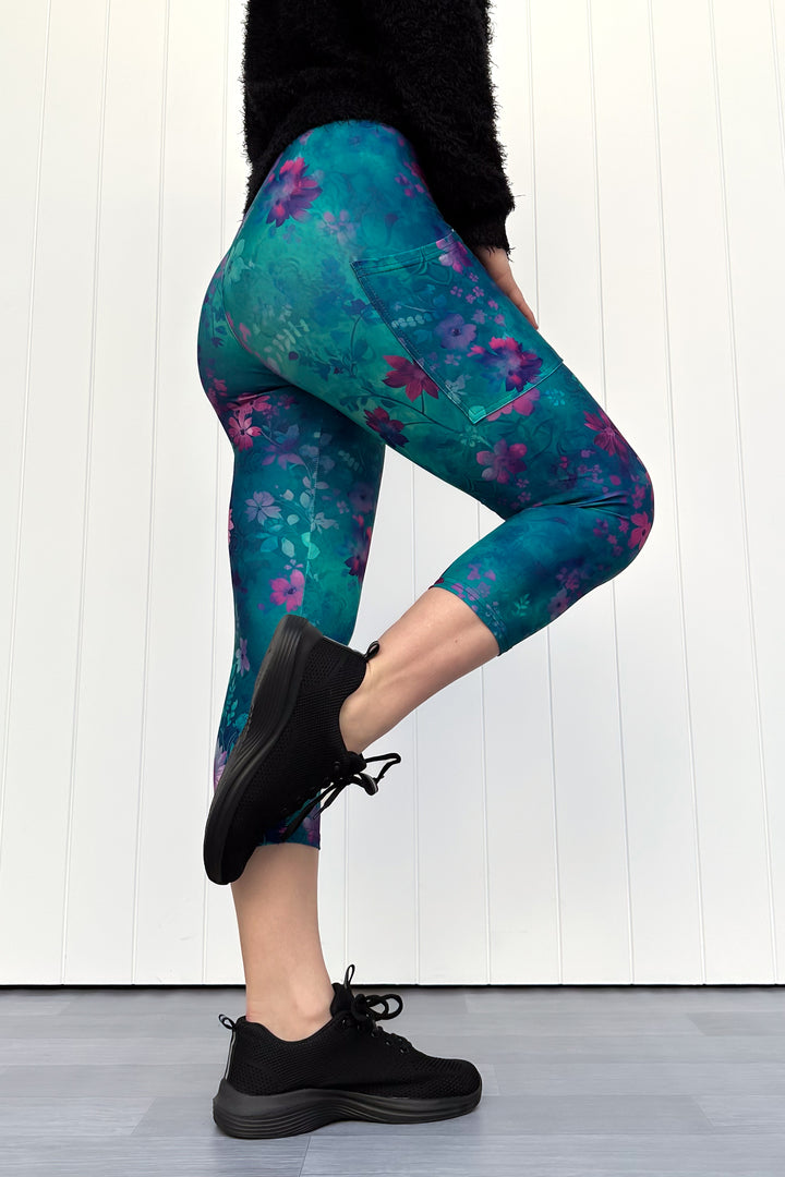 Person wearing teal leggings with purple floral pattern and black sneakers on a white background