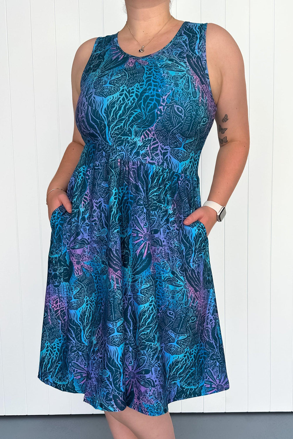 A model wearing a sleeveless knee-length dress with a multicolored animal print and side pockets.