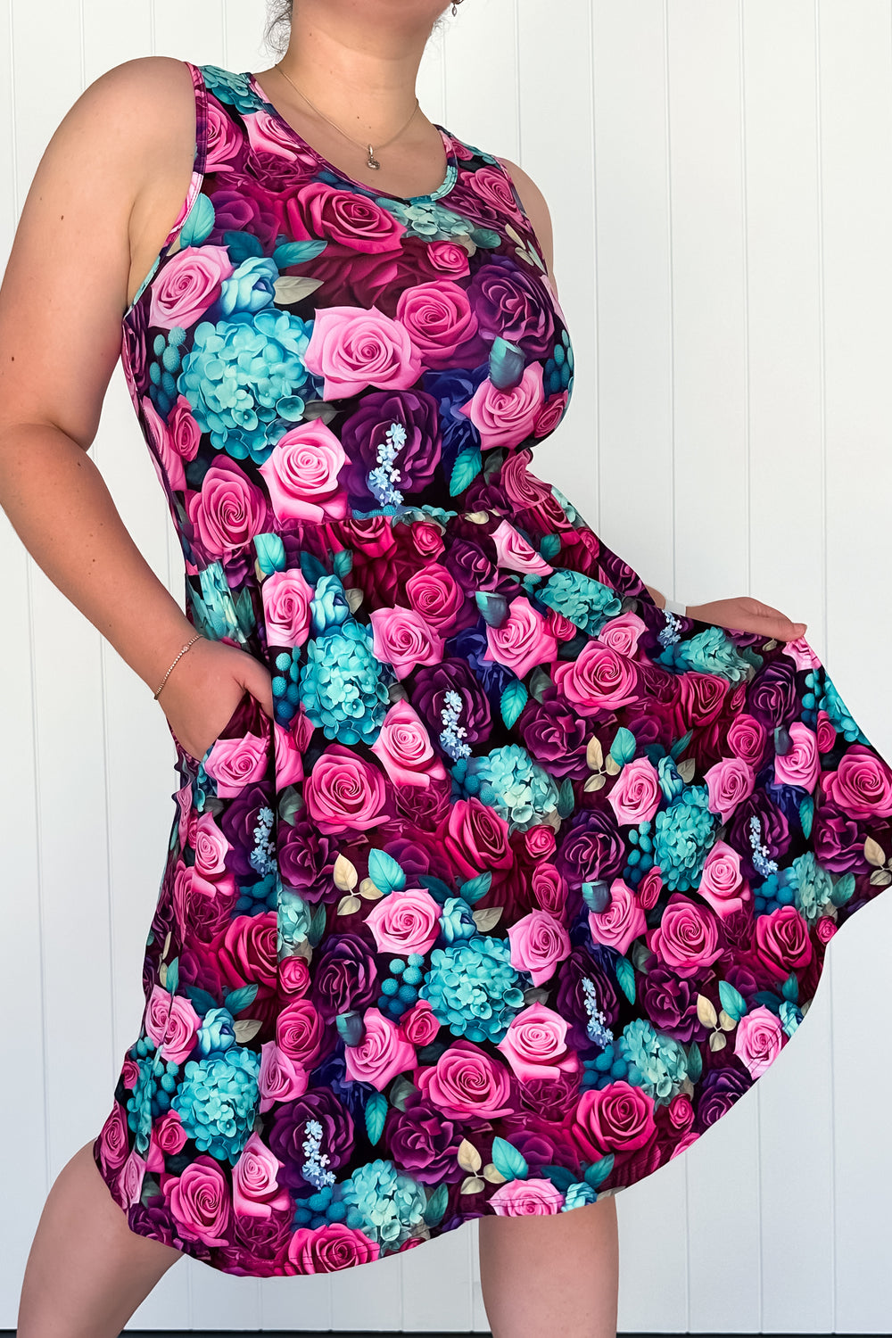 A sleeveless knee-length dress with a floral pattern in shades of pink, purple, and blue, featuring side pockets.