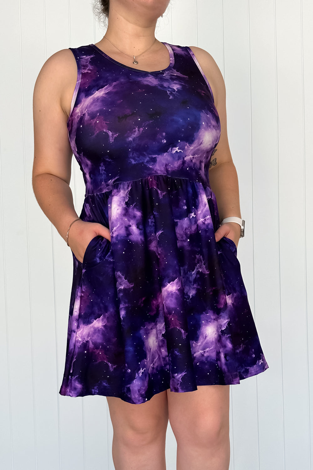 A sleeveless mini dress with a printed pattern resembling a galaxy or space-themed design in purple and blue tones. The dress has a round neckline and two side pockets.