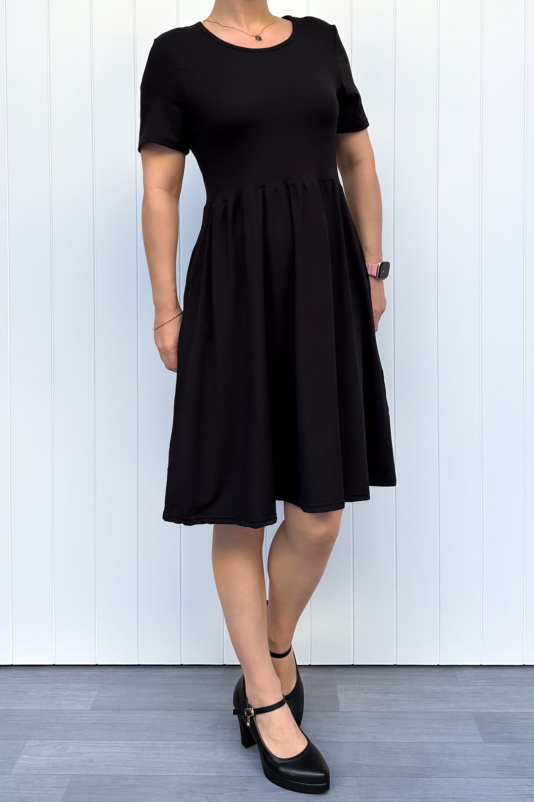 Woman wearing a black dress against a white wooden panel background