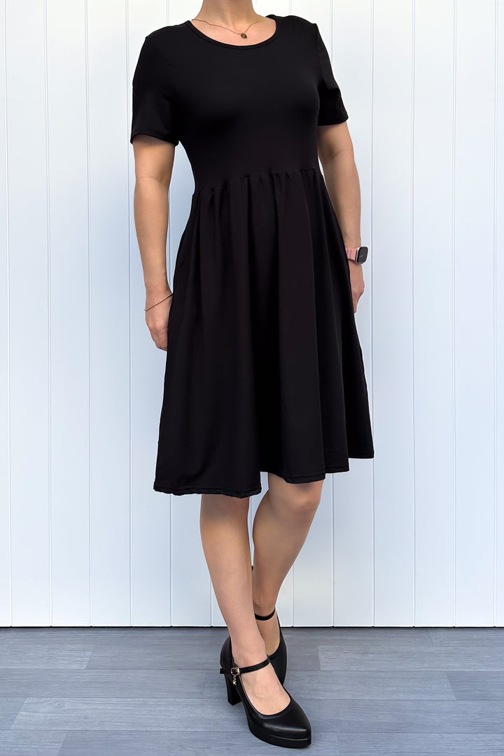 Woman wearing a black dress against a white wooden panel background