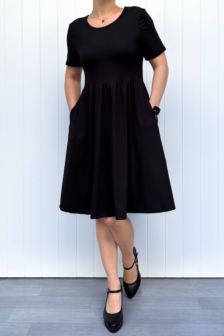 Woman wearing a black, short sleeve, knee length dress against a white background