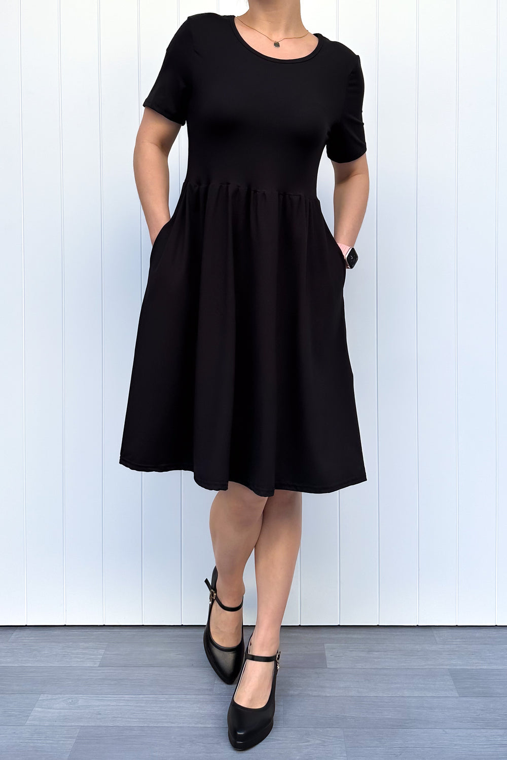 Person wearing a black dress standing against a white wooden panel background