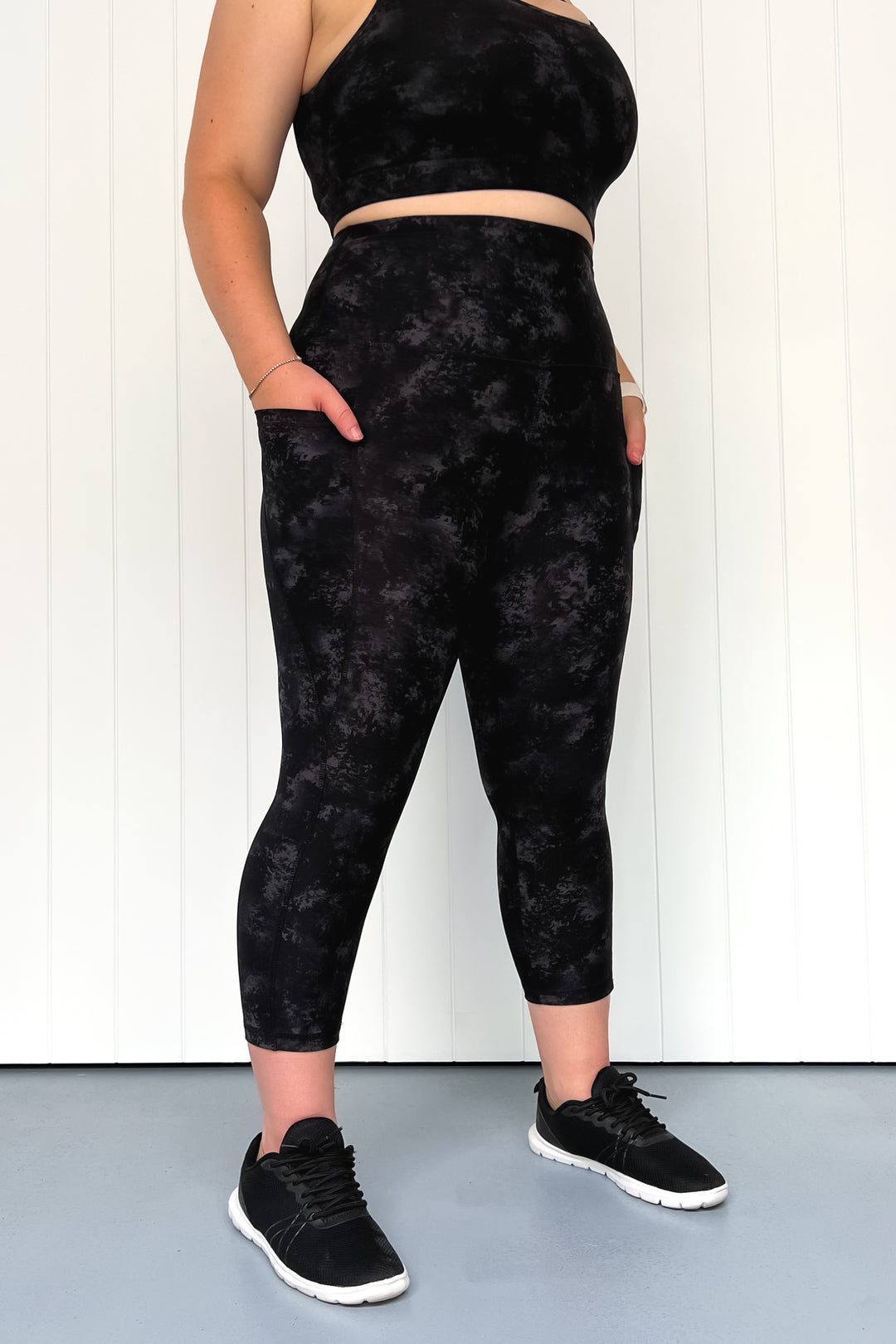 Person wearing black tie-dye leggings and crop top against a white background