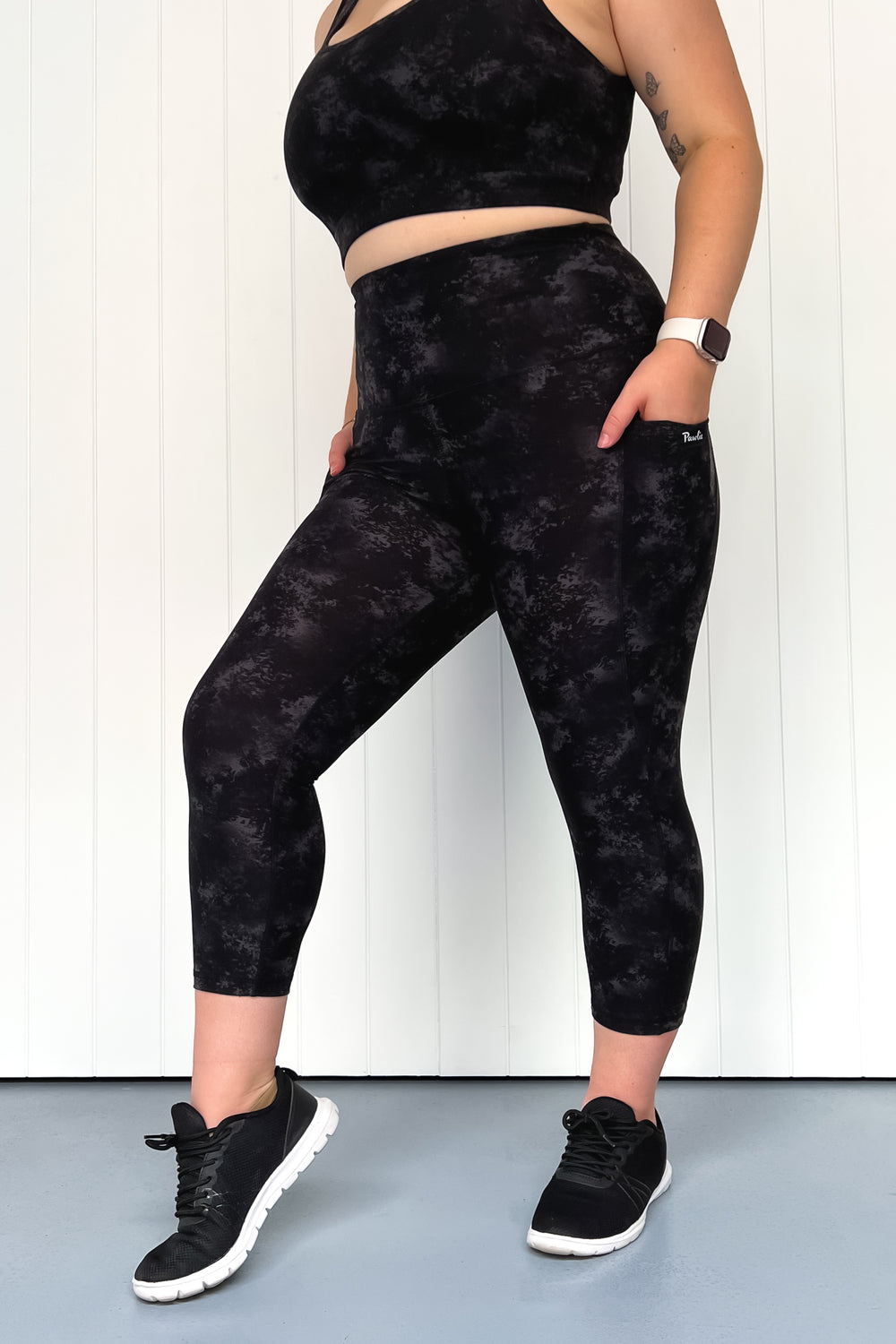Person wearing black tie-dye leggings and crop top against a white wall.