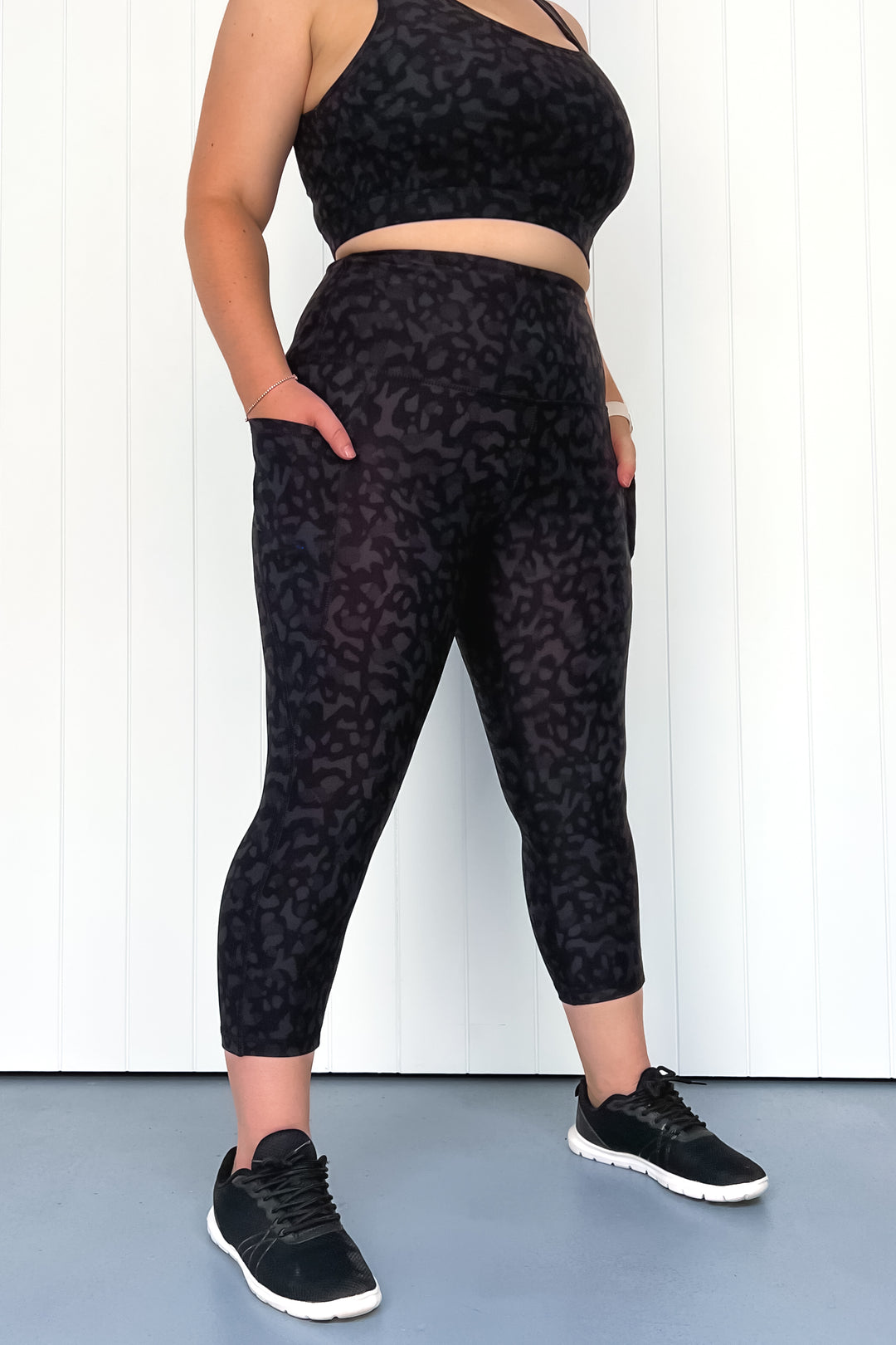 Person wearing black leopard print athletic pants and crop top on a white background