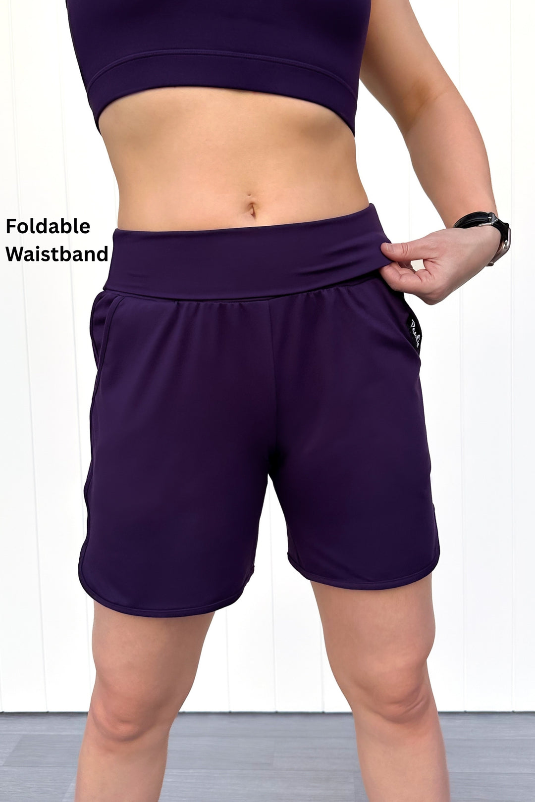 Person wearing purple athletic shorts with a foldable waistband on a white background