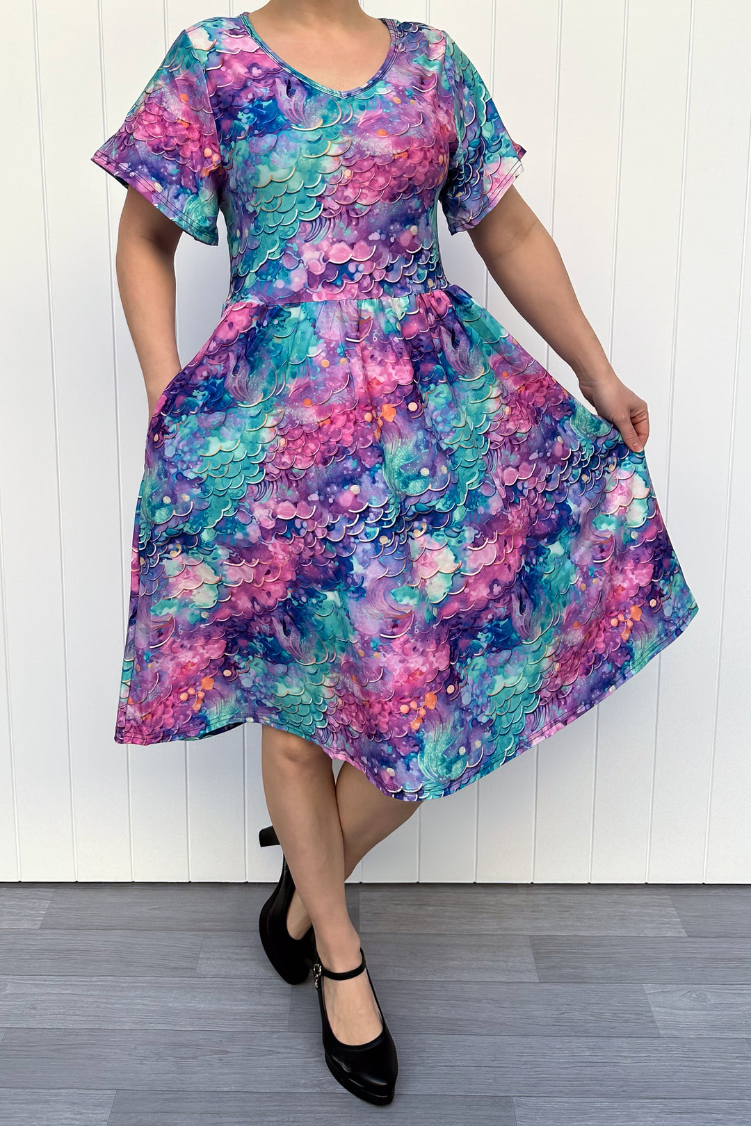 Person wearing a colourful mermaid siren pattern dress against a white wooden panel background