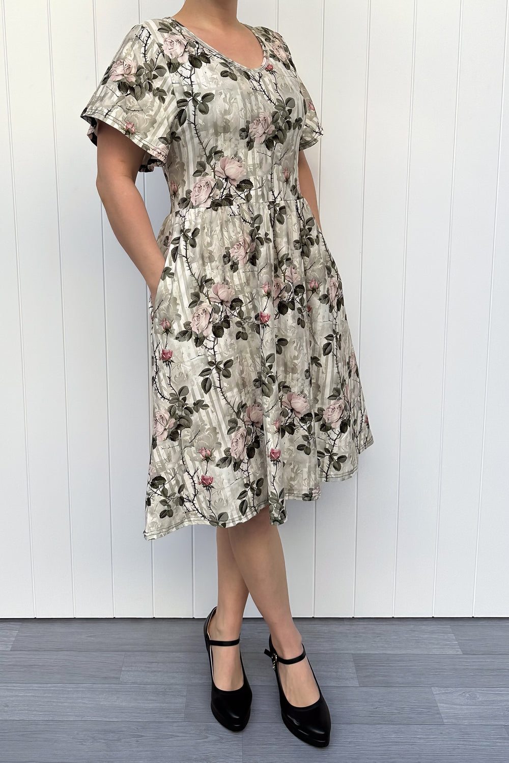 Woman wearing a floral dress standing against a white wooden panel background