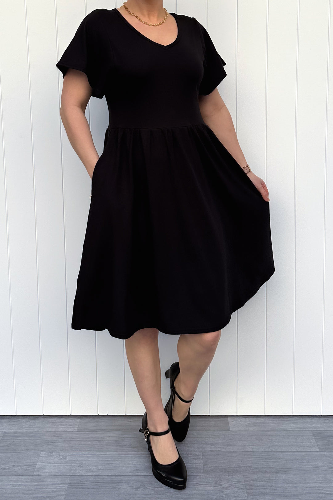 Person wearing a black dress standing against a white wooden panel background