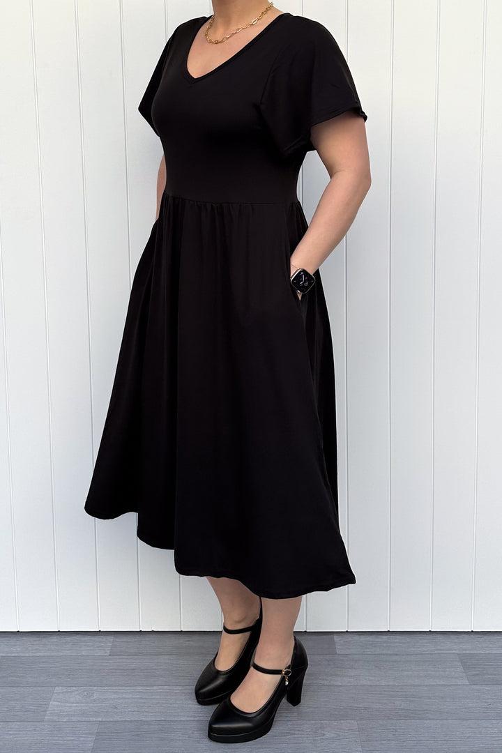 Person wearing a black dress against a white wooden panel background