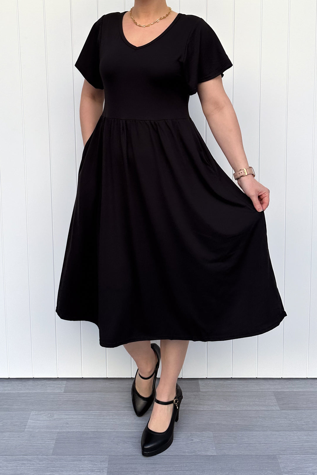 Person wearing a black dress against a white wooden panel background