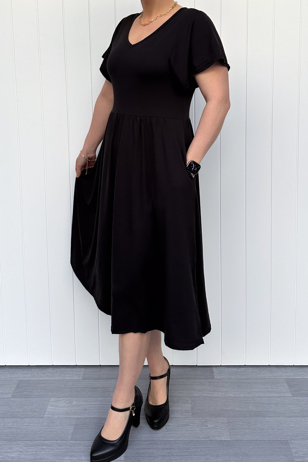 Person wearing a black dress standing against a white wall.