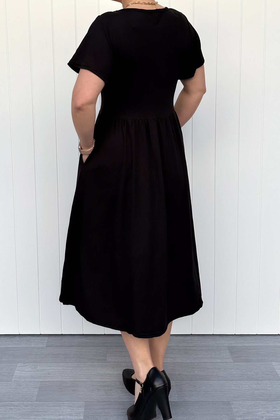 Person wearing a black dress standing against a white wall.