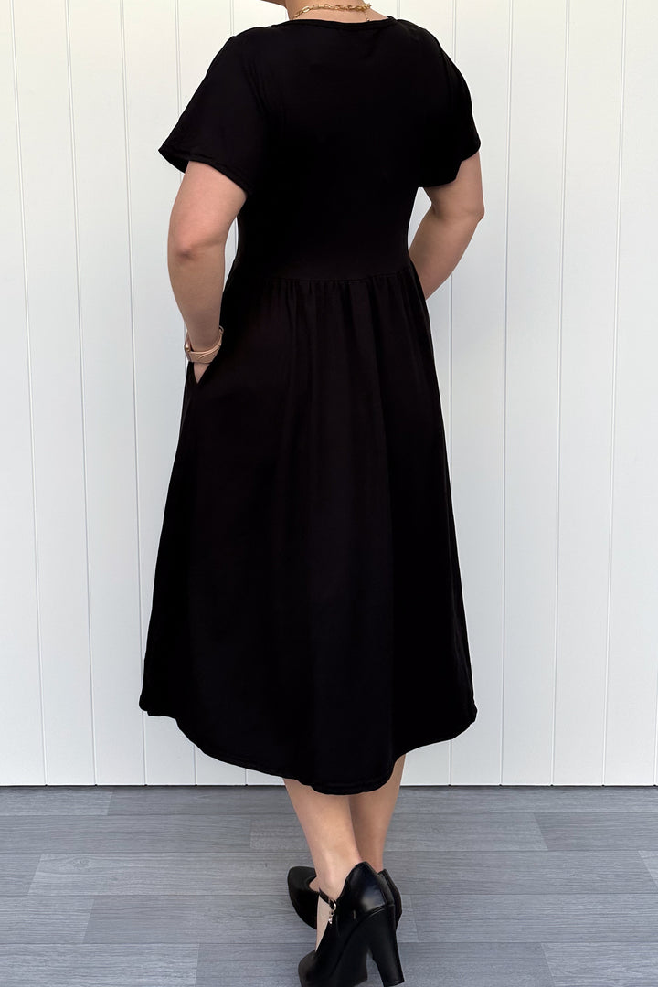 Person wearing a black dress standing against a white wall.