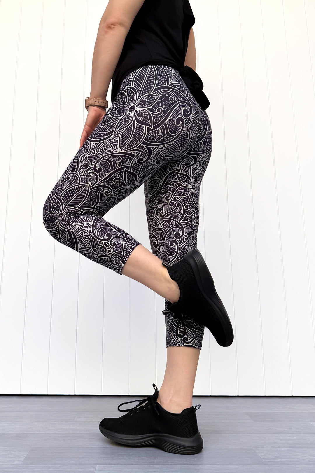 Person wearing black and white patterned leggings with black shoes on a white wooden floor.