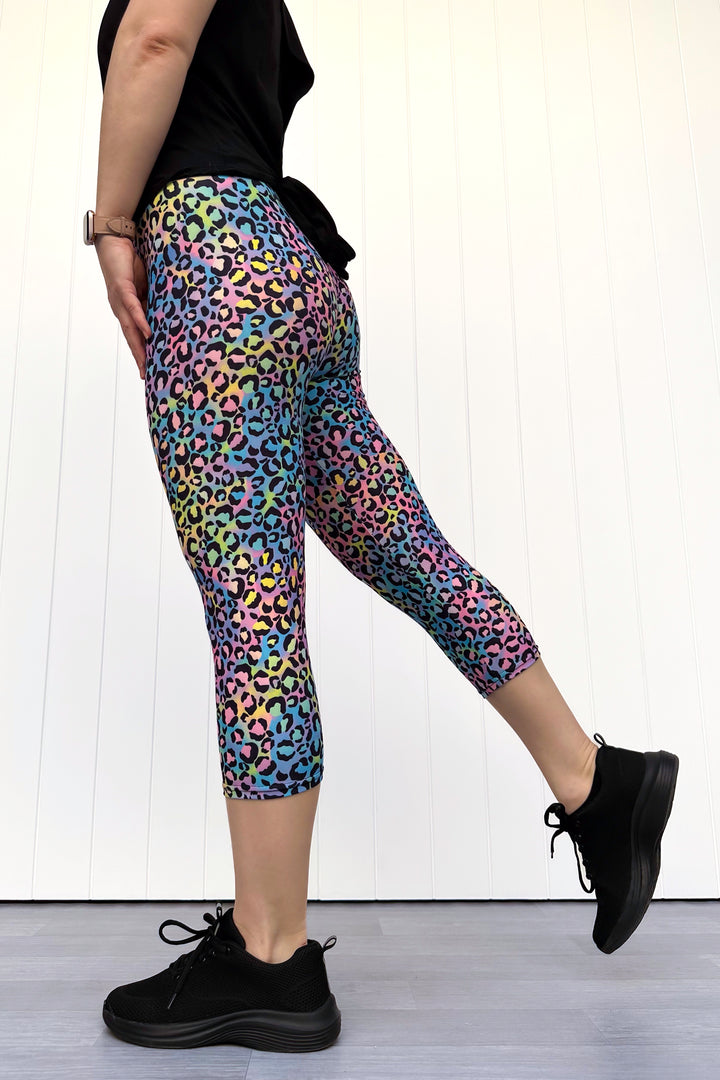 Person wearing colorful leopard print leggings with black shoes on a white background