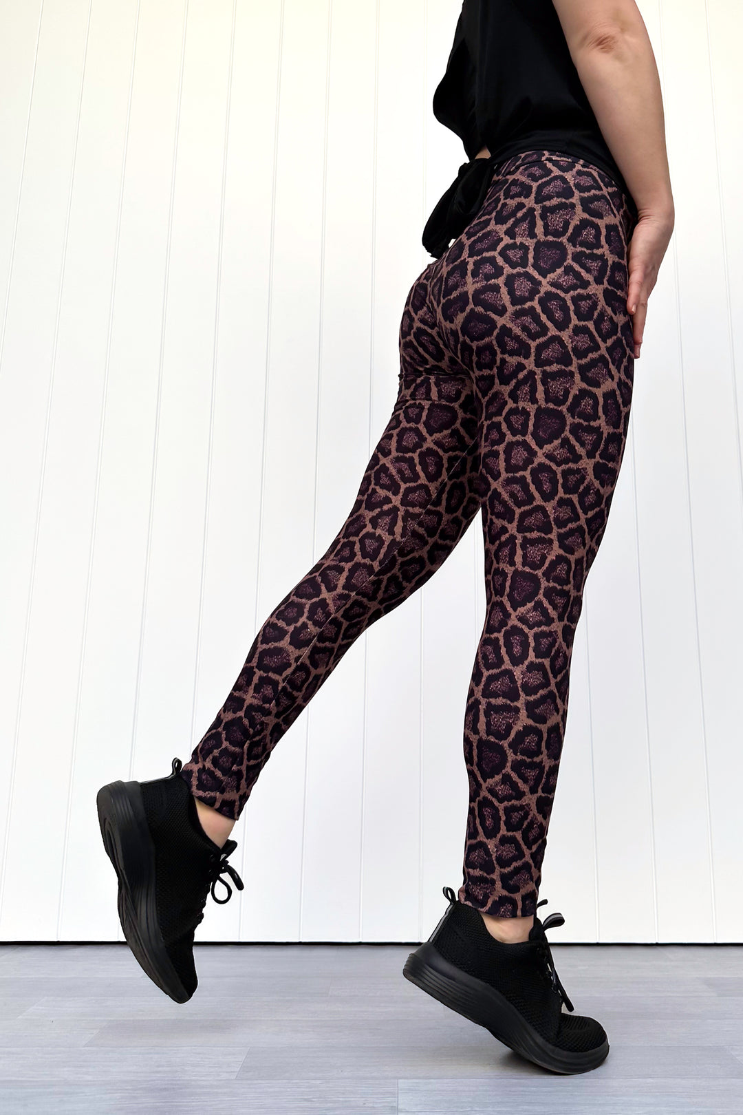 Person wearing leopard print leggings and black shoes on a white background