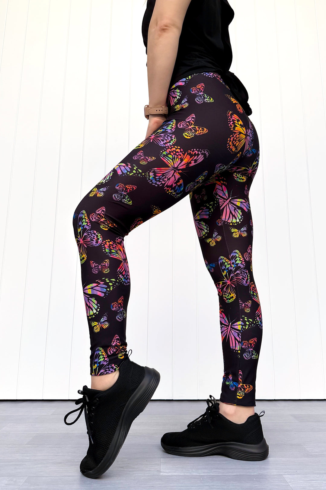 Person wearing black leggings with colorful butterfly pattern on a white background