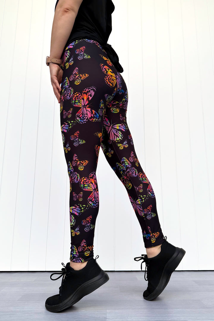Person wearing black leggings with colorful butterfly pattern against a white background
